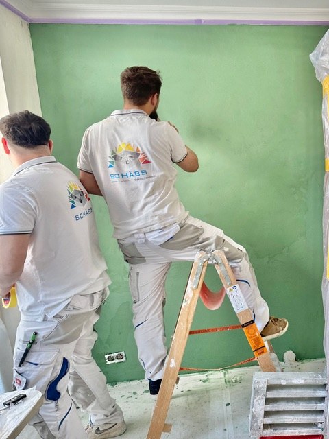 Zwei Kollegen von Schäbs bei Malerarbeiten an einer grünen Wand